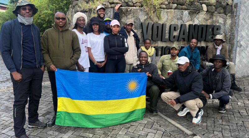 Tourists taking photos beside the Visit Rwanda and Volcanoes National Park sign post, highlighting Rwandan adventure tourism with Explore More Tours.