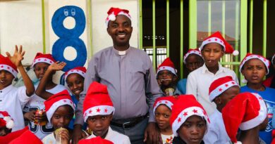 Pastor Jean Bosco HABINSHUTI and students wearing Christmas hats smiling together outside Nyamata Christian Academy in Bugesera