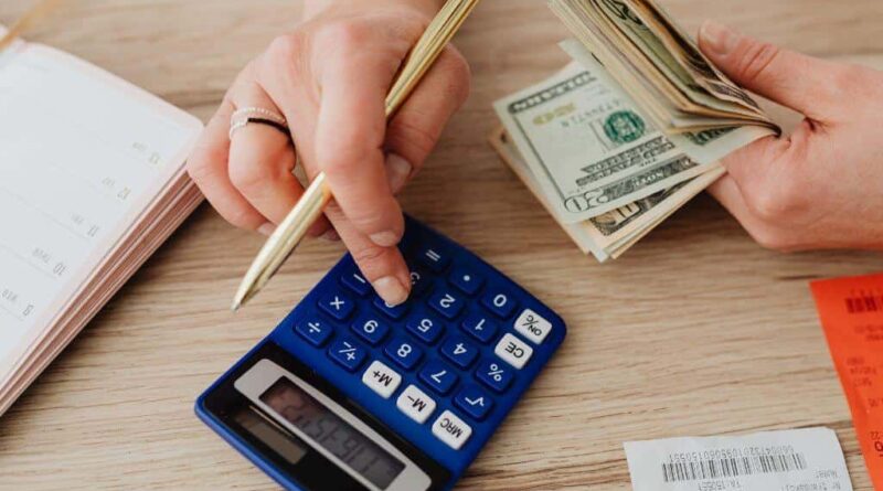 Person actively managing their monthly salary, counting money with a calculator and pencil to track expenses and plan savings.