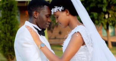 Bride Donatha MUKESHIMANA in a white wedding dress and groom Elie NSENGIMANA in a white suit and black pants, smiling together on their wedding day at ADEPER Church Nyamata.